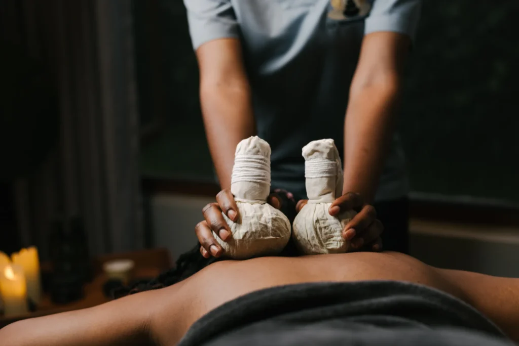 Therapist pressing herbal compresses along a guest's back by candlelight