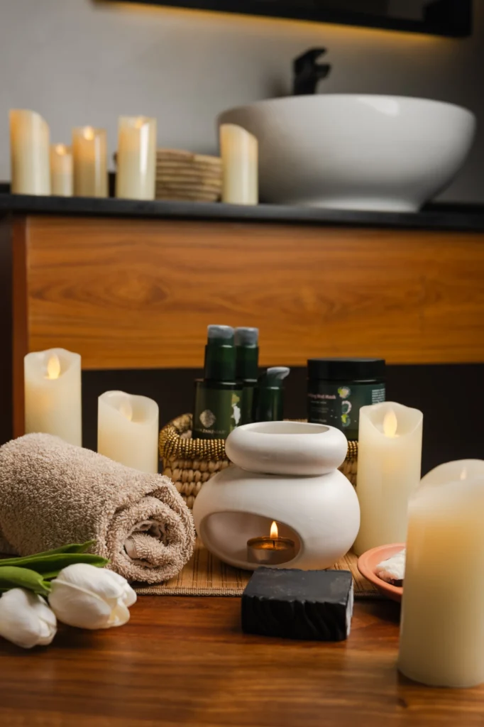 Candles, an oil burner, rolled towel and spa products beside a basin